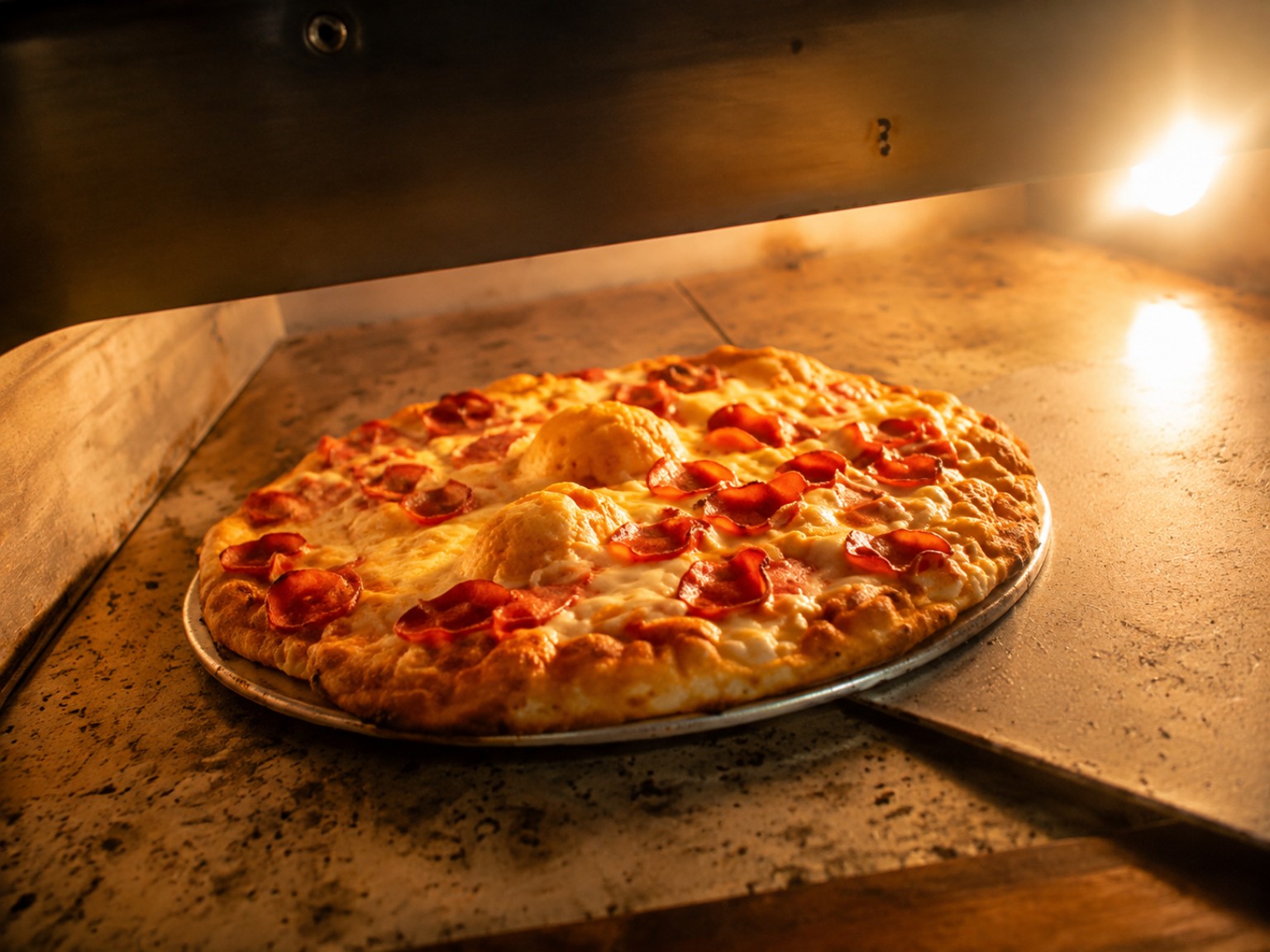 Pizza con queso fundido y embutido sobre una bandeja metálica dentro del horno